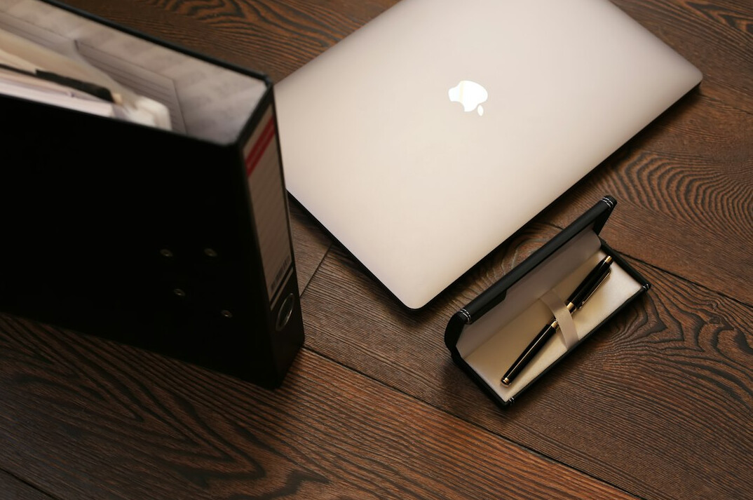 Overhead view of a desk with a laptop, notebook and pen